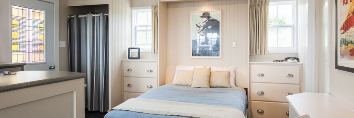 Cozy bedroom with a neatly made bed, light-colored curtains, soft blue bedding, and a stylish decor featuring wall art and drawers.