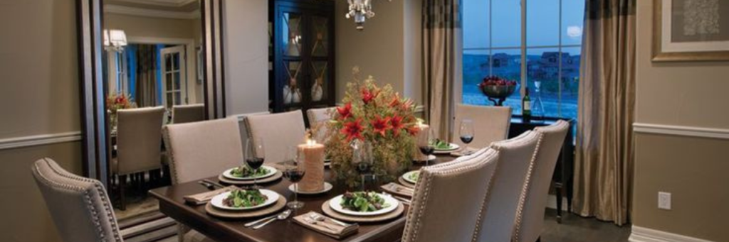 Elegant dining room with a beautifully set table, upholstered chairs, floral centerpiece, warm lighting, and floor-to-ceiling curtains