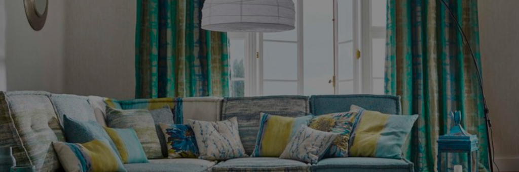 A living room featuring a blue and green color scheme with patterned upholstery and matching curtains, along with decorative cushions and a cozy ambiance.