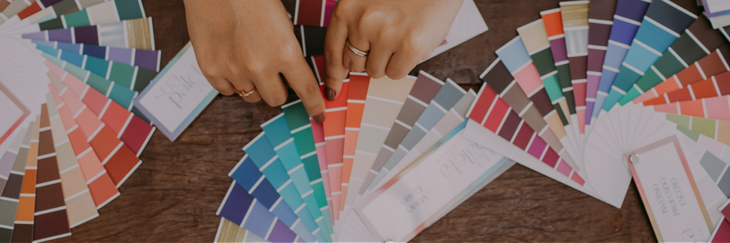 Two hands are sorting through colorful paint swatches on a wooden table, showcasing a vibrant array of color palette.