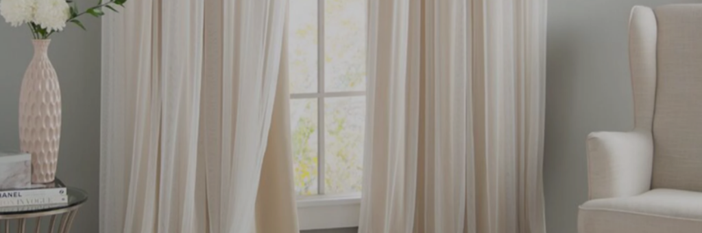 Bright room with sheer cream curtains, a pink vase with white flowers, and a stylish side table beside a beige armchair.