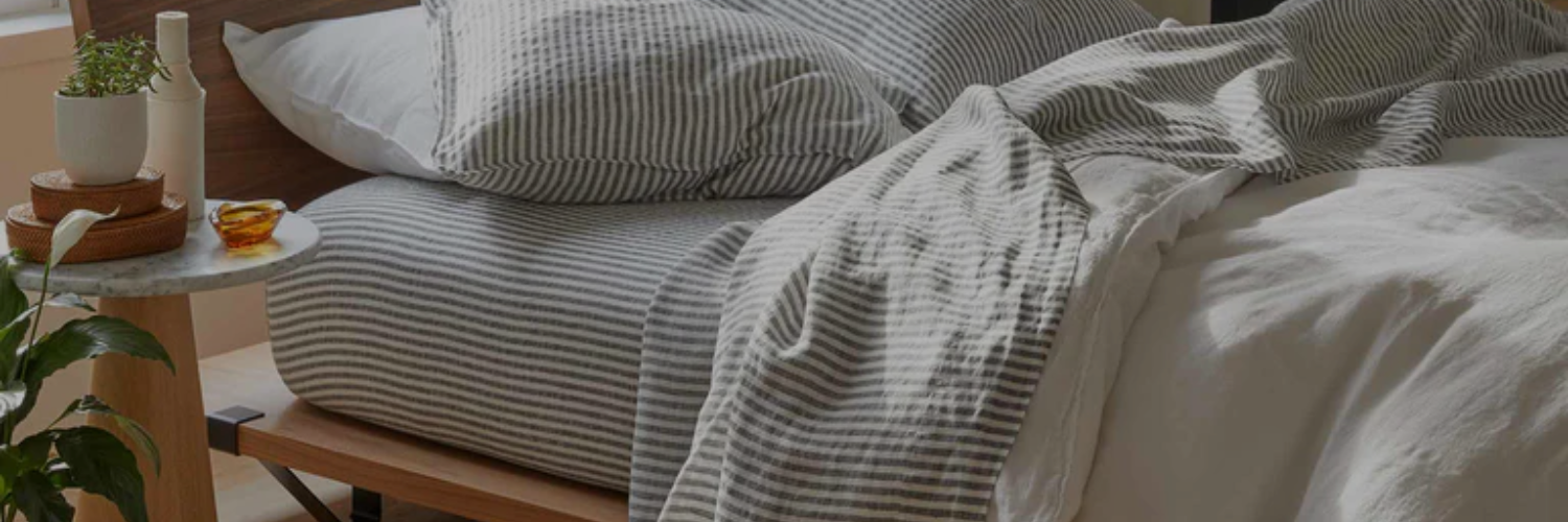 A neatly made bedding with striped pillows and blanket, alongside a marble-topped side table with a plant and small decor items.