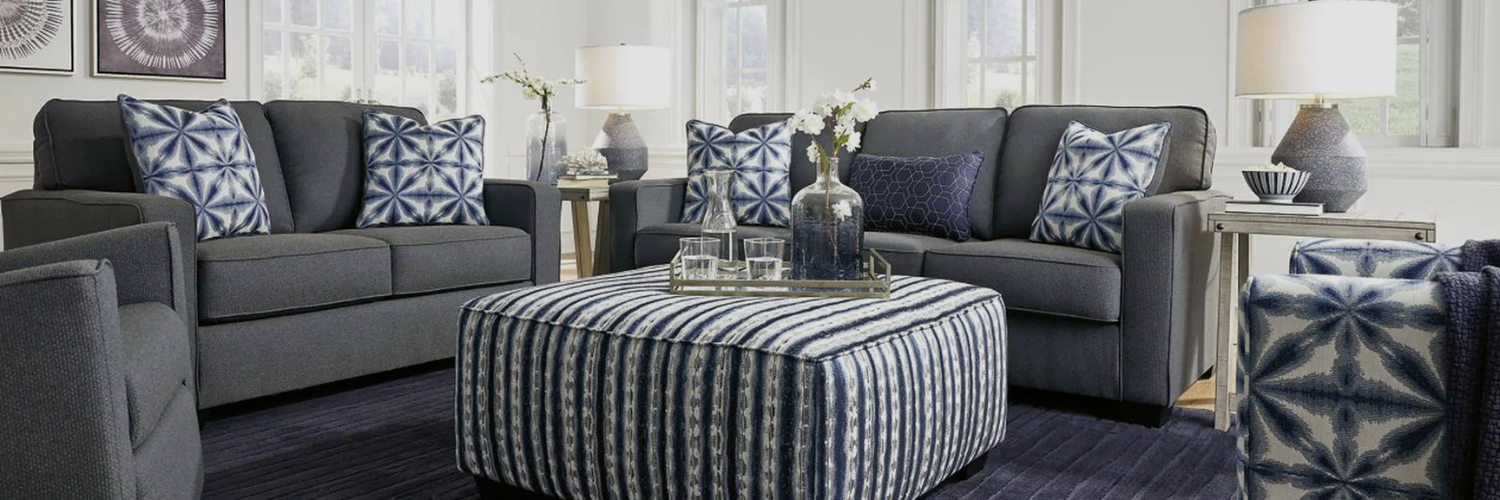 Modern living room featuring dark gray sofas with blue-patterned pillows, a striped ottoman, and stylish decor elements.