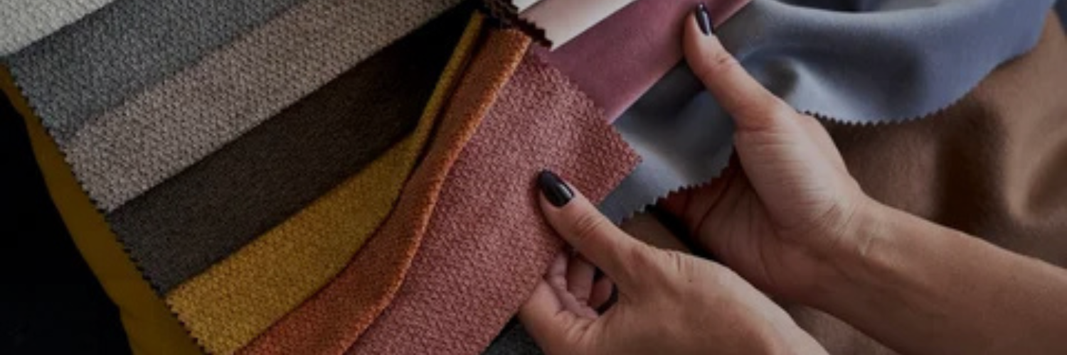 Two hands hold colorful upholstery fabric swatches, showcasing various textures and hues of textile materials arranged in a fan shape.