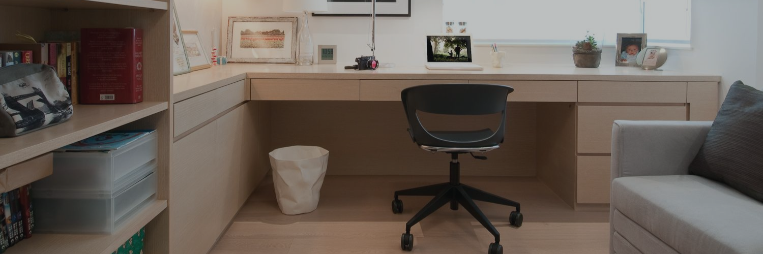 A minimalistic workspace featuring a wooden desk, black chair, bookshelves, and decorative items, set in a bright room with natural light.