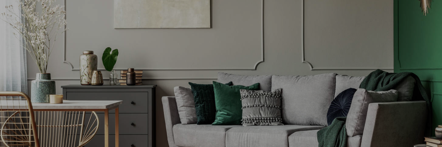 A cozy living room featuring a gray sofa with colorful pillows, a wooden dining table, and decorative vases against a muted green wall.