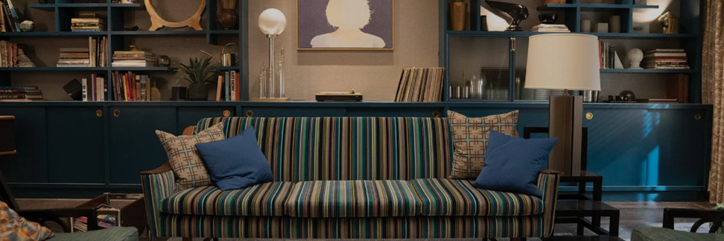 A stylish living room featuring a striped sofa, blue bookcase filled with books, and modern lighting, creating a cozy atmosphere.