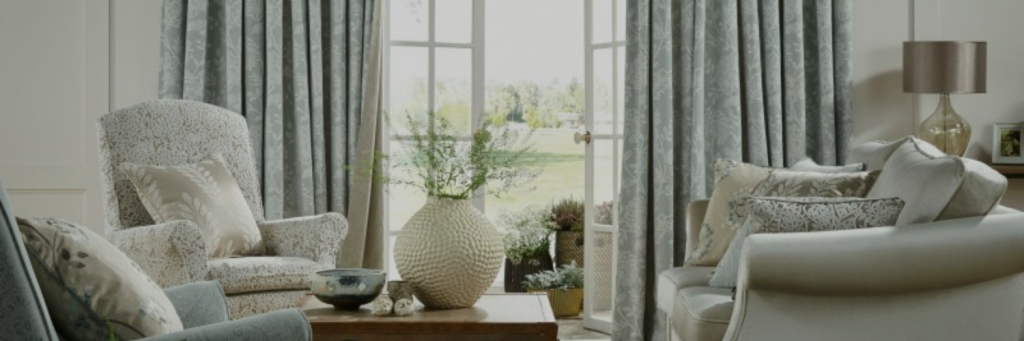 Cozy living room featuring patterned curtains, elegant armchairs, and a large vase with greenery, bathed in natural light.