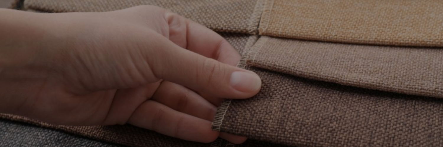 A hand examines fabric swatches in various earthy tones, showcasing textures and colors for potential selection.