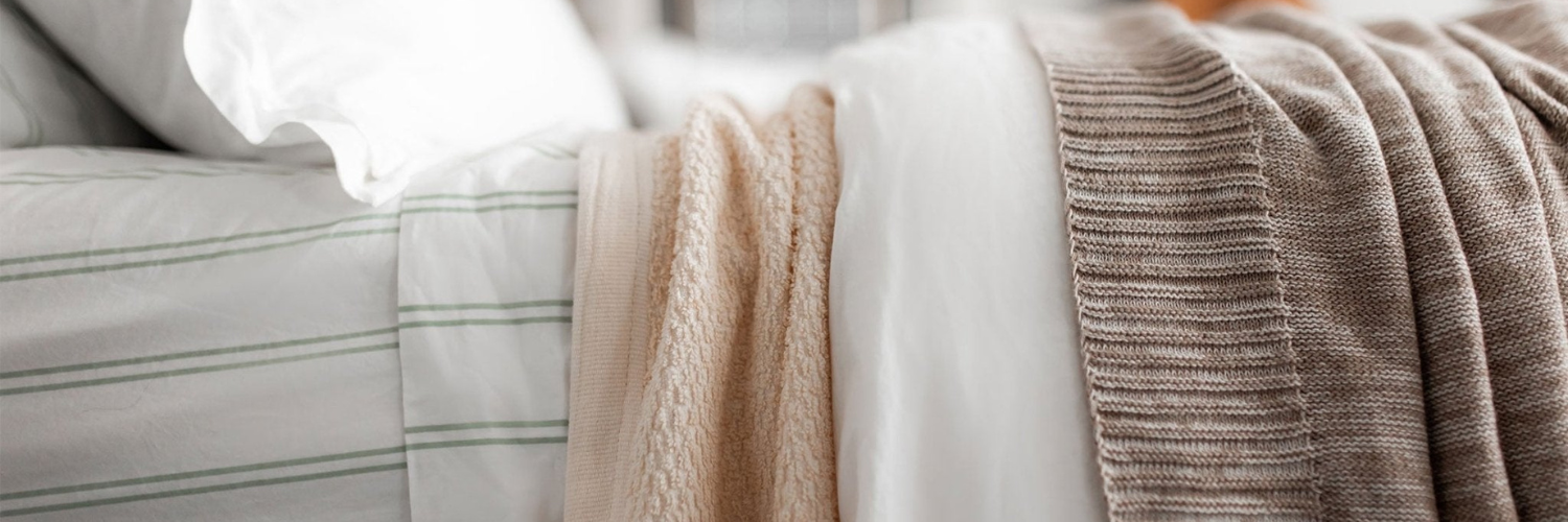 Close-up of a neatly made bed with white, striped, and textured beige blankets and a white pillow.