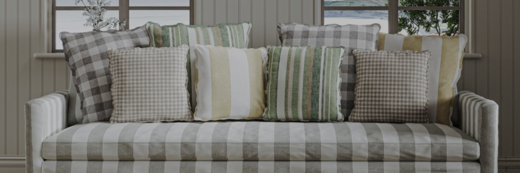 Sofa with grey and white stripes, adorned with various green, beige, and grey patterned throw pillows, in front of a window with plants outside.