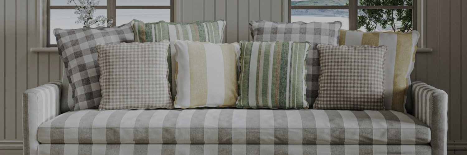 Sofa with grey and white stripes, adorned with various green, beige, and grey patterned throw pillows, in front of a window with plants outside.