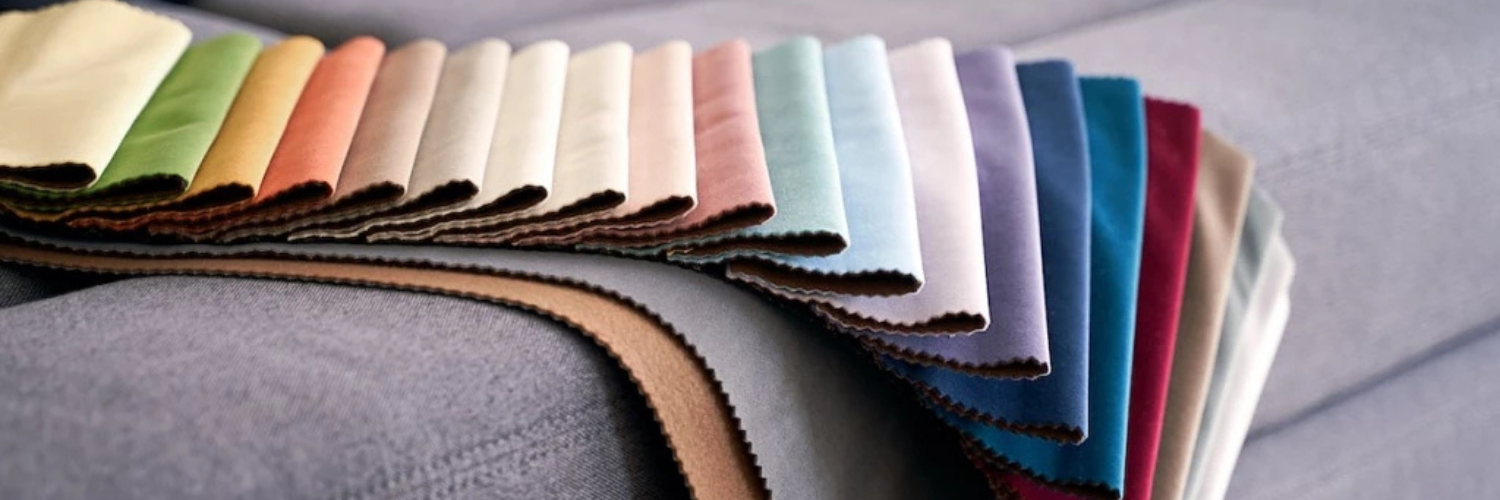 A row of colorful fabric swatches is spread out on a gray upholstered surface, showcasing a wide range of shades from cream and brown to blue and burgundy.